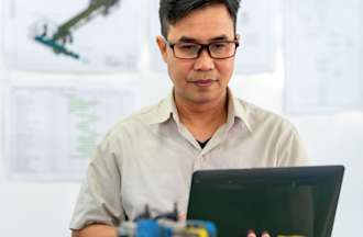 [Featured Image] A controls engineer examines his computer in front of a wall of mechanical diagrams.