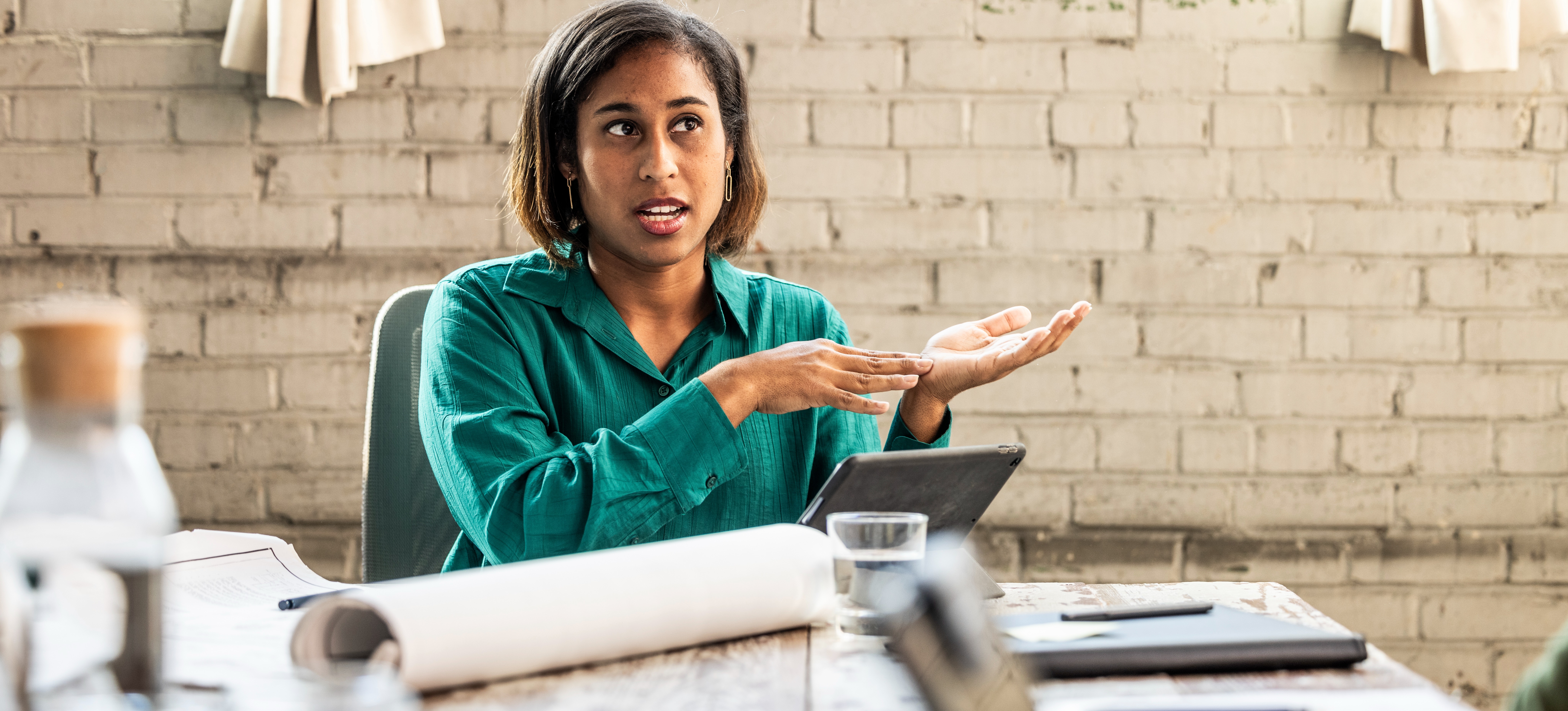 [Featured Image] A reporting analyst sits at a table in a meeting room and explains data insights to their colleagues. 