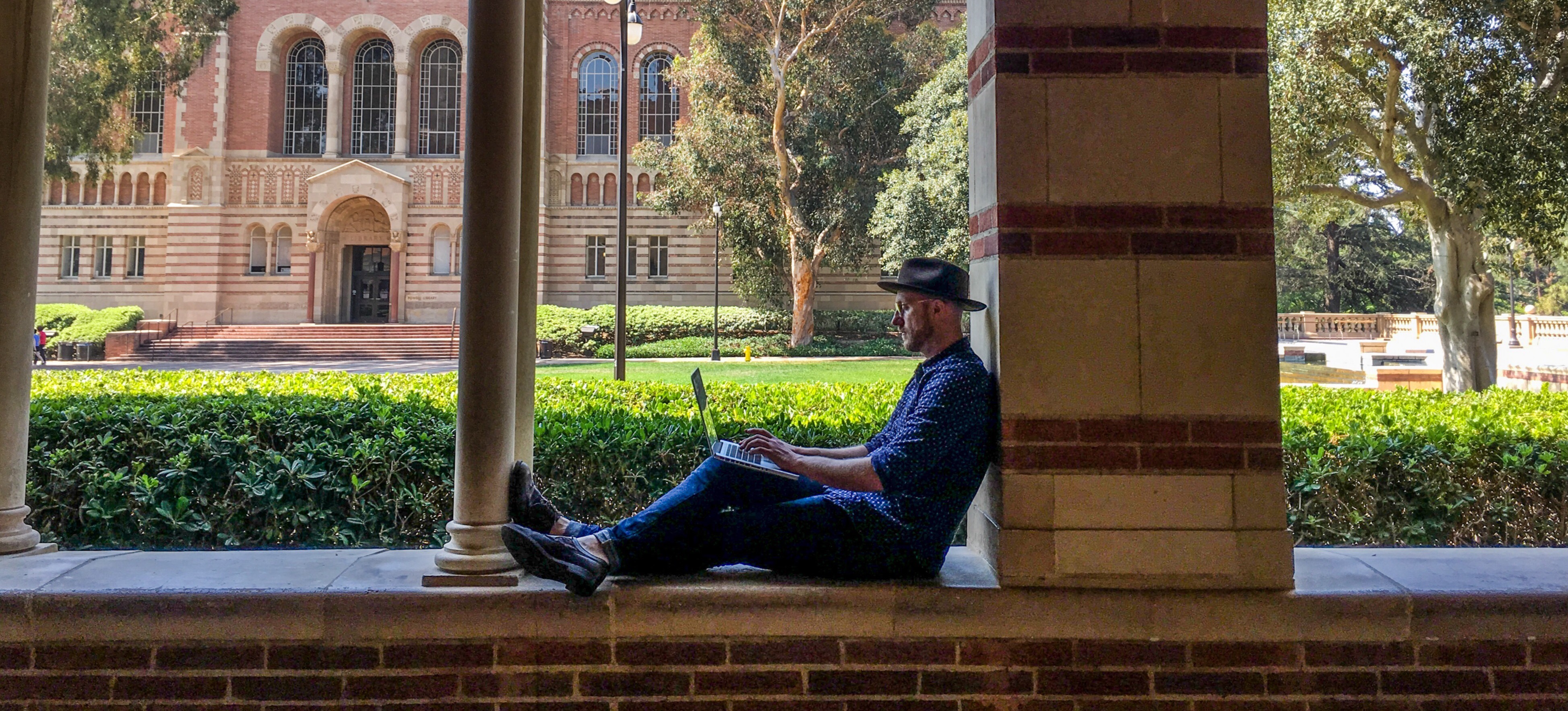 [Featured image] A person working on getting their master's degree studies on a laptop outside on a university campus.