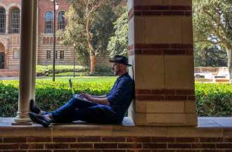 [Featured image] A man working on getting his master's degree studies on a laptop outside on a university campus.