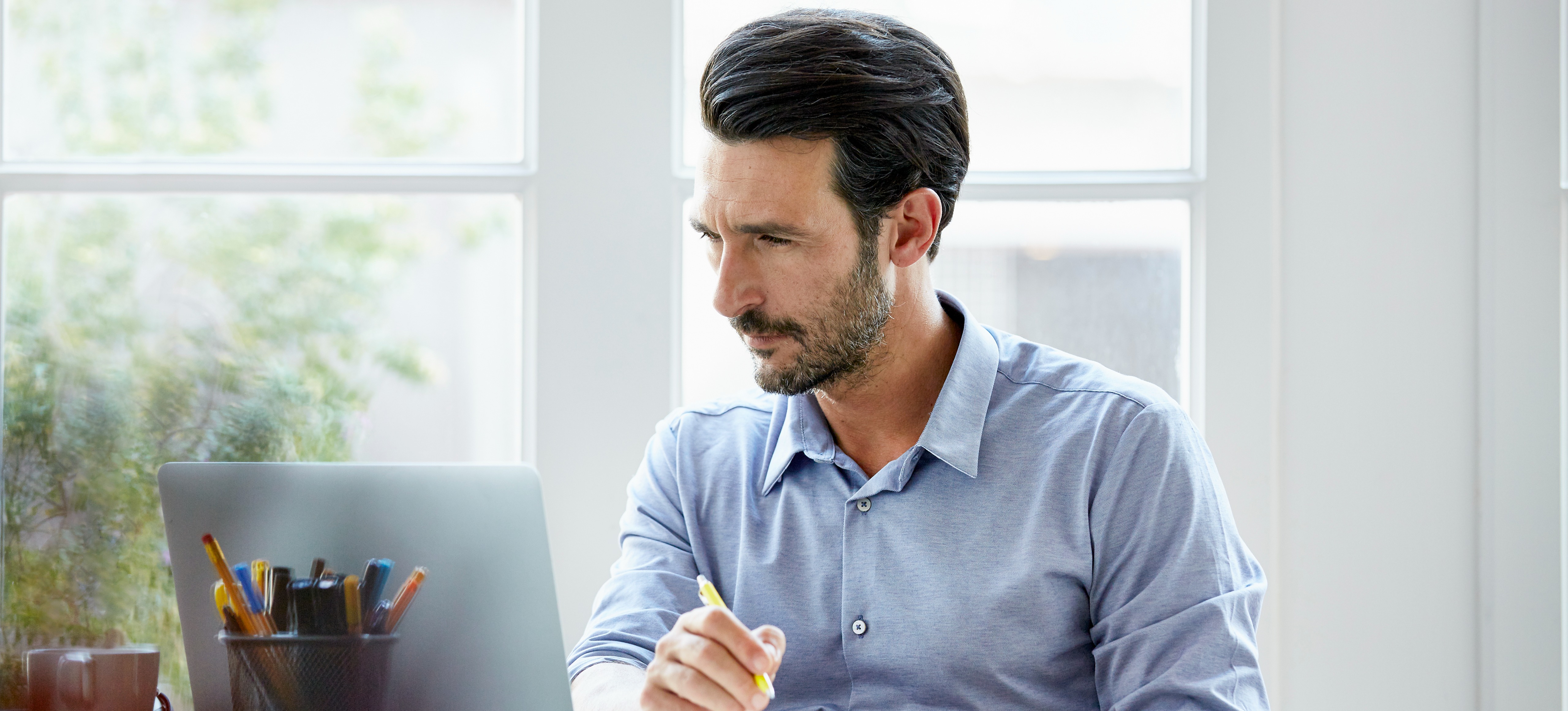 [Hauptbild] Ein Mann sitzt mit seinem Laptop in seinem Büro und recherchiert „Was ist Cloud Native?“.
