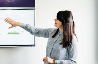 [Featured Image]: A female health informatics specialist presents data on a large screen. 