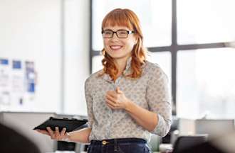 [Featured Image] A project manager is in business casual clothing and is facing her two coworkers while holding a tablet. 