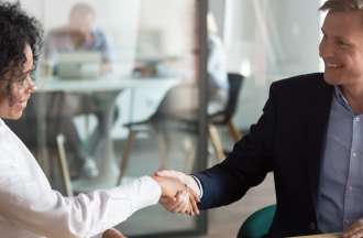 [Featured image] A tech salesperson shaking hands with a client in an office after just closing a deal.
