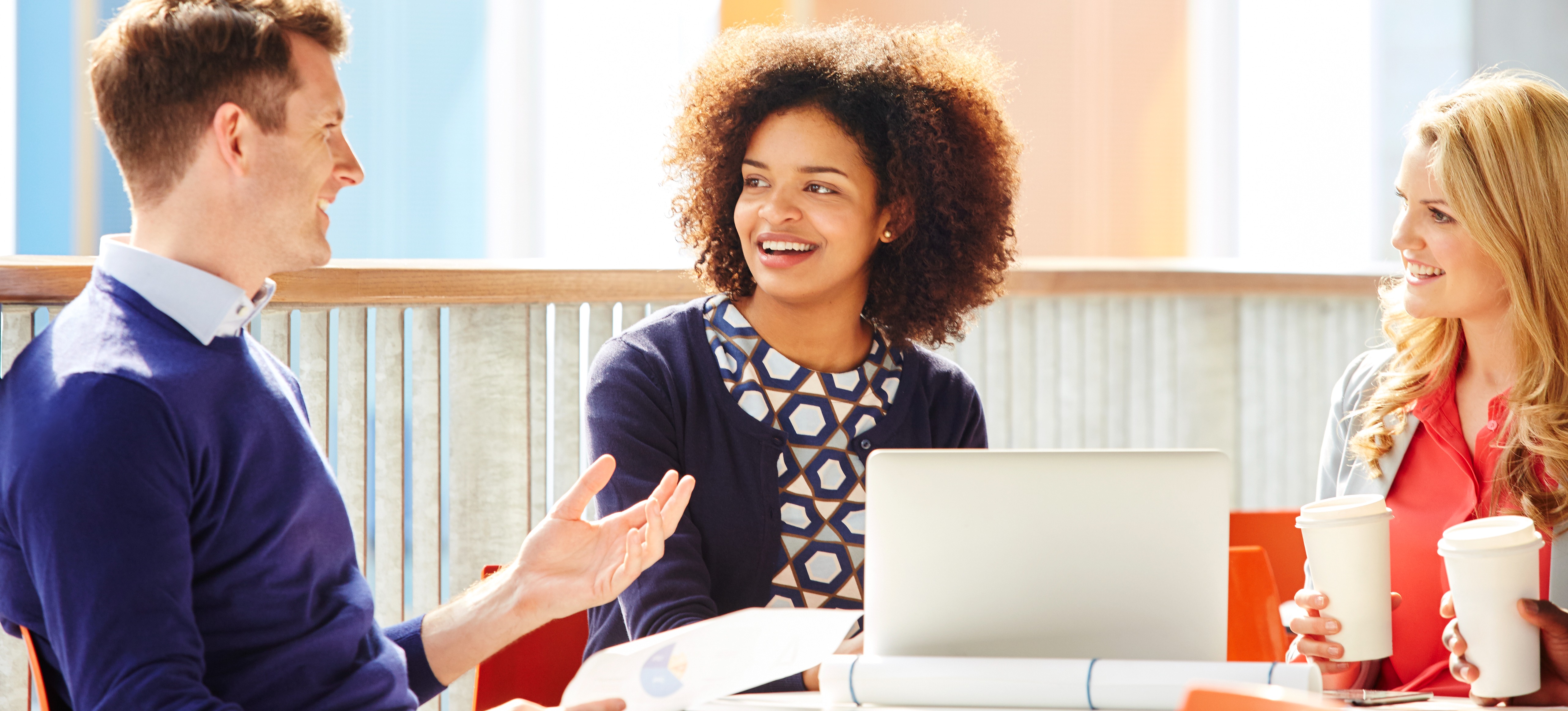 [Featured Image] A group of employees sit around a laptop and drink coffee while discussing IaaSvs PaaS vs SaaS. 