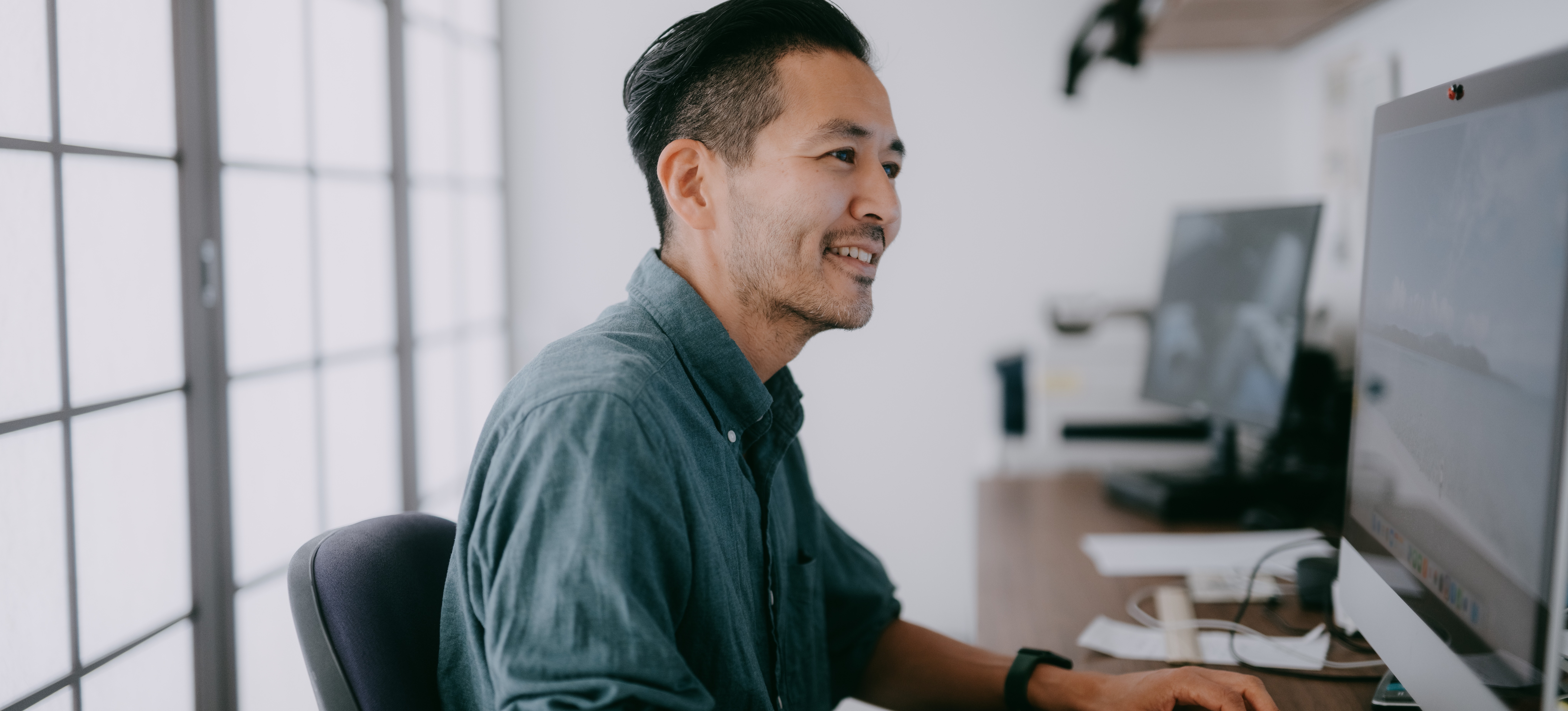 [Featured Image] A smiling machine learning engineer in a green button-down shirt works at their computer on a natural language processing project.
