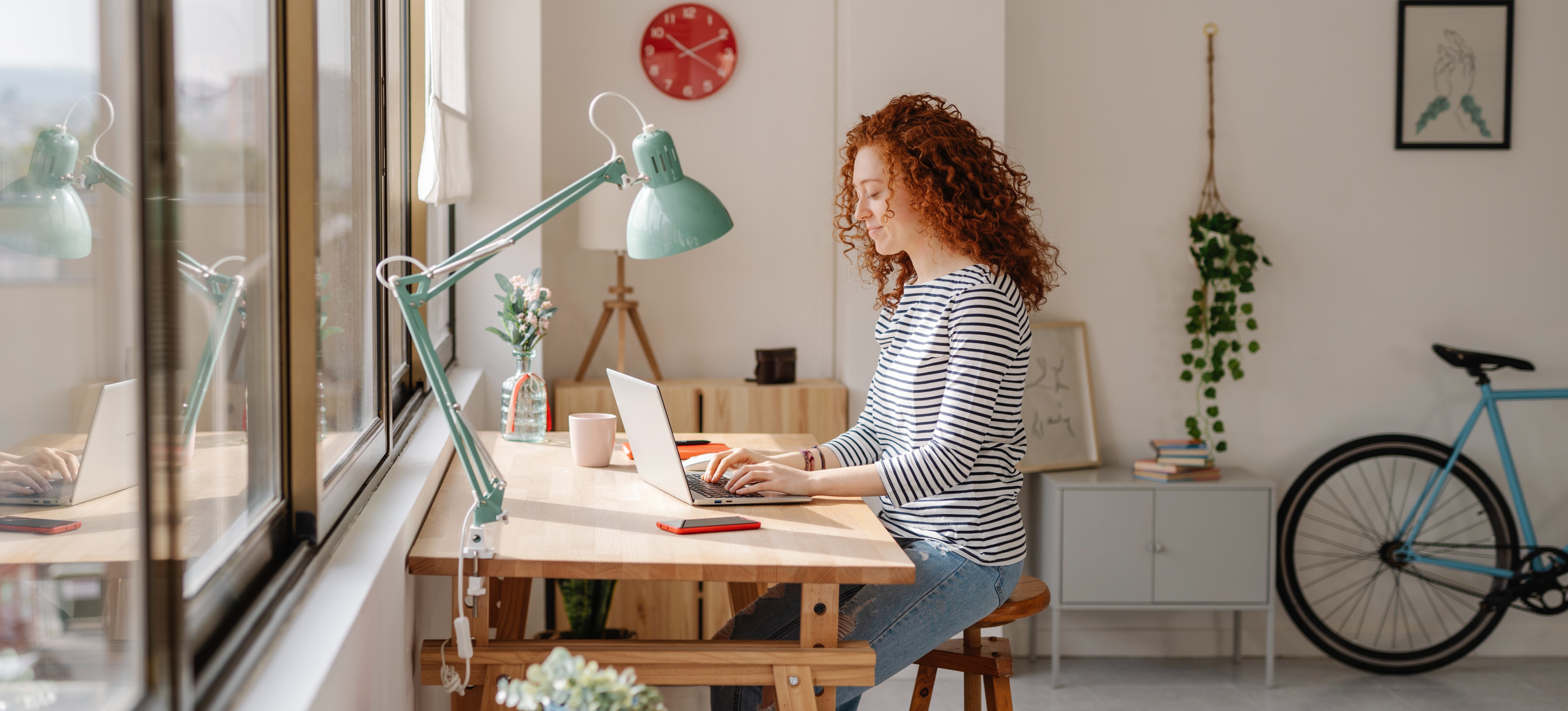 [Hauptbild] Eine Frau mit roten Locken lächelt, während sie in ihrem Heimbüro auf ihrem Laptop das OSI-Modell studiert.