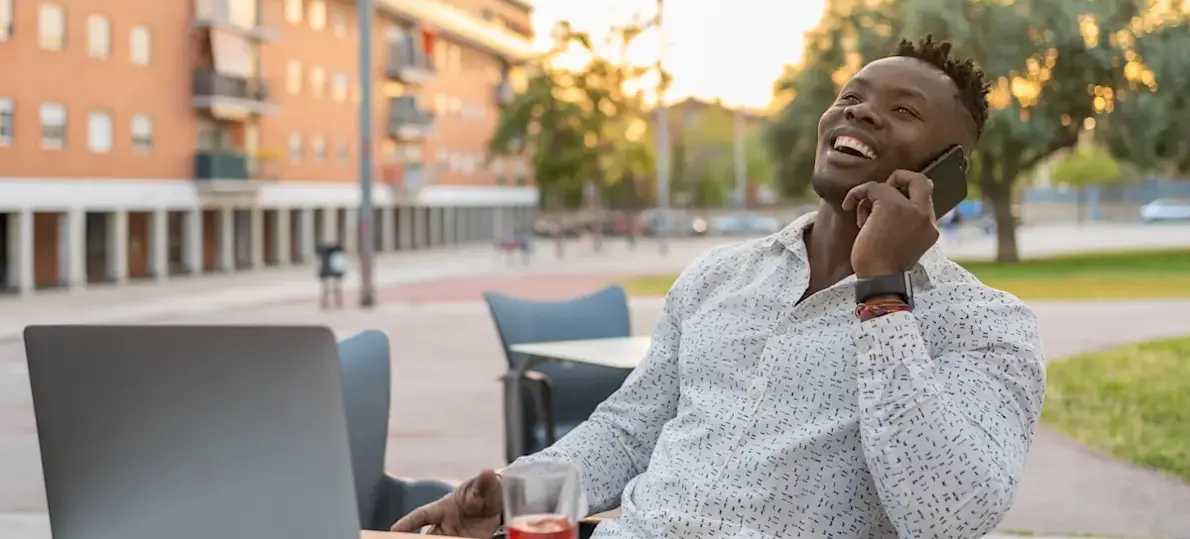 [Featured Image] A businessperson sits outside the office building with their laptop and talks on the phone with a colleague about potential LLM use cases they can use to automate the customer experience.
