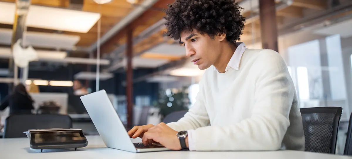 [Featured image] A UX designer is working on their laptop while in an office. 