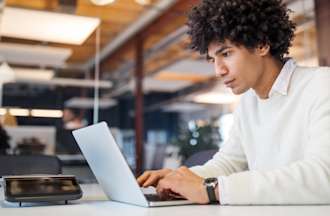 [Featured image] A UX designer is working on their laptop while in an office. 