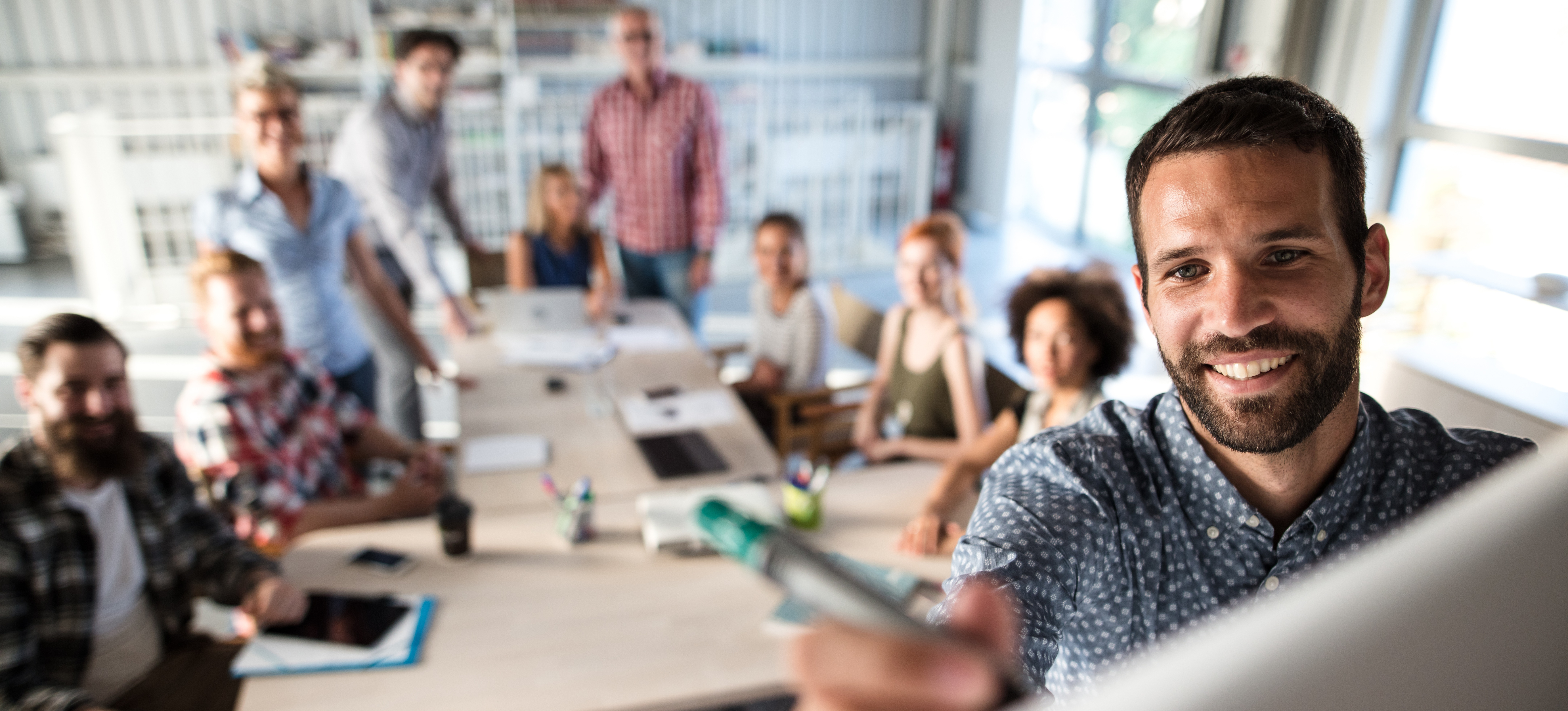 [Featured Image] A smiling social media manager writes on a whiteboard while his team of colleagues looks on in the background.
