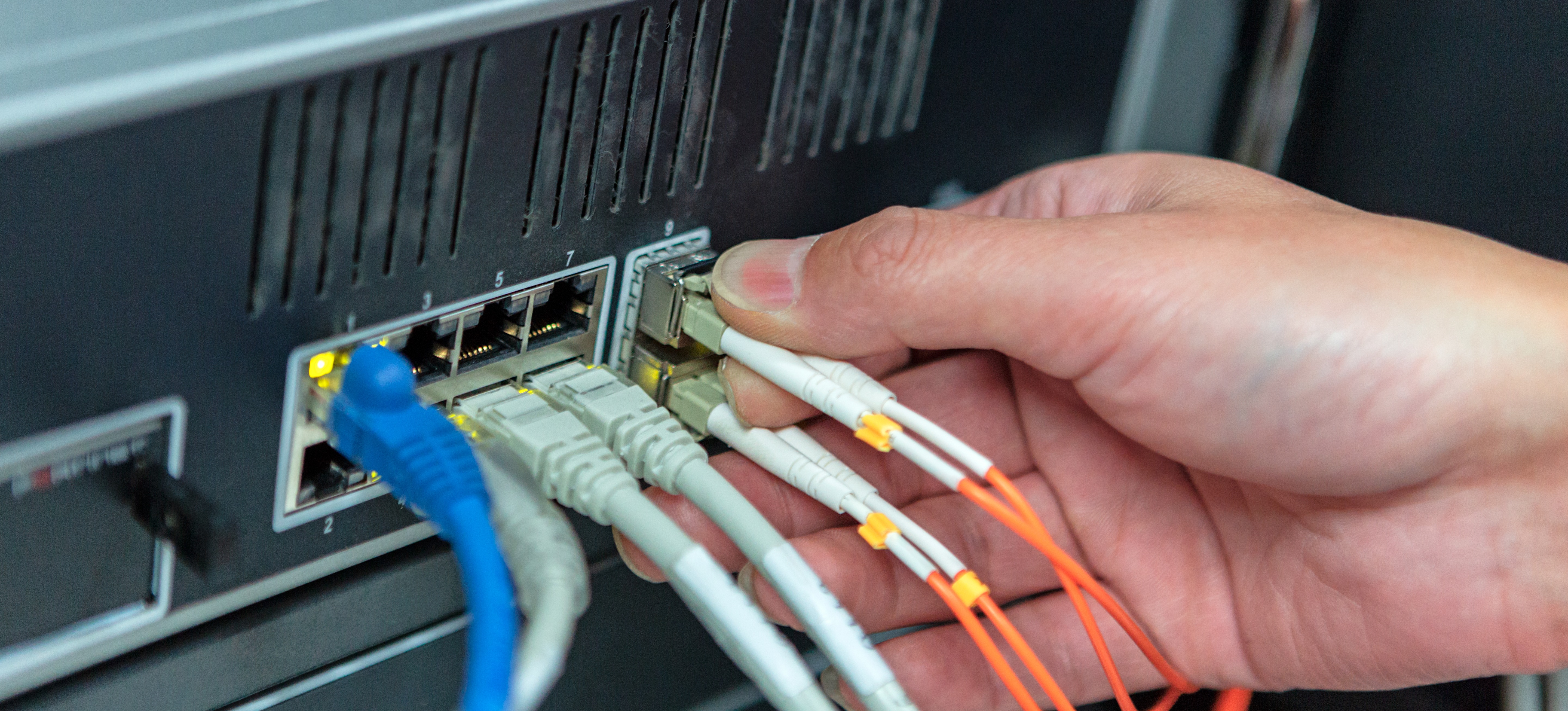 [Featured Image] The hands of a technical support agent are plugging in cables to a server to build a business intelligence architecture for a company.