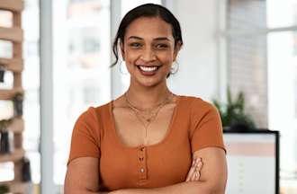 [Featured image] A young woman of color in a burnt orange top stands with her arms crossed, smiling at the camera. 