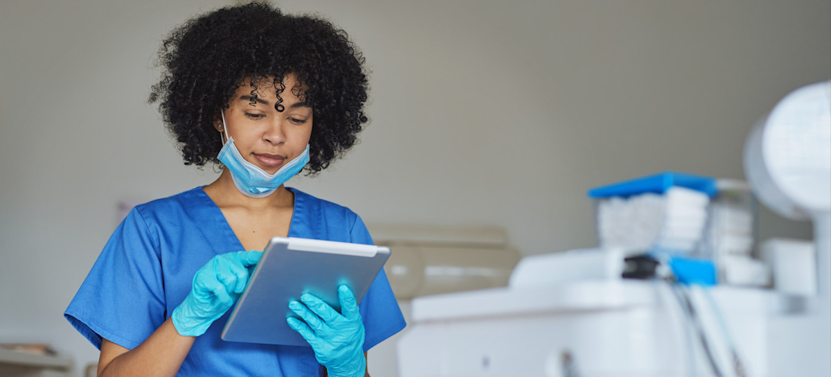 [Featured Image] A dental hygienist works in a dentist's office on a tablet.