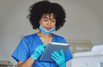 [Featured Image] A female dental hygienist works in a dentist's office on a tablet.