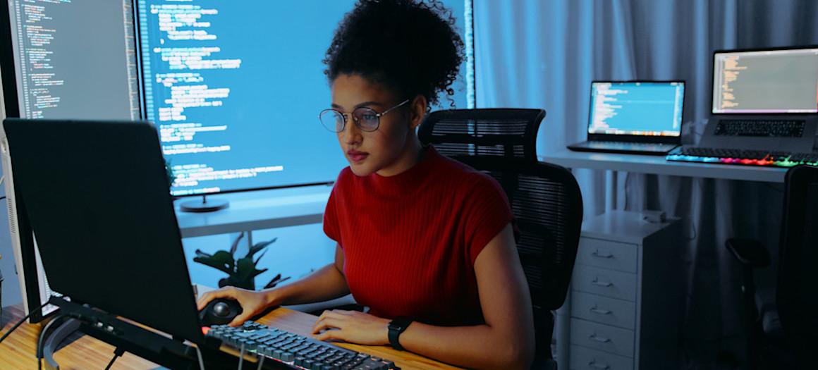 [Featured Image] A cybersecurity professional interested in advancing their career studies for CompTIA CySA+ certification in an office with multiple computer monitors.
