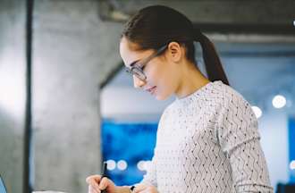 [Featured image] A quality assurance technician in a white shirt takes notes while working in front of a laptop computer.