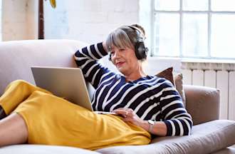 A person smiling while lounging on a couch attending online school on a laptop.