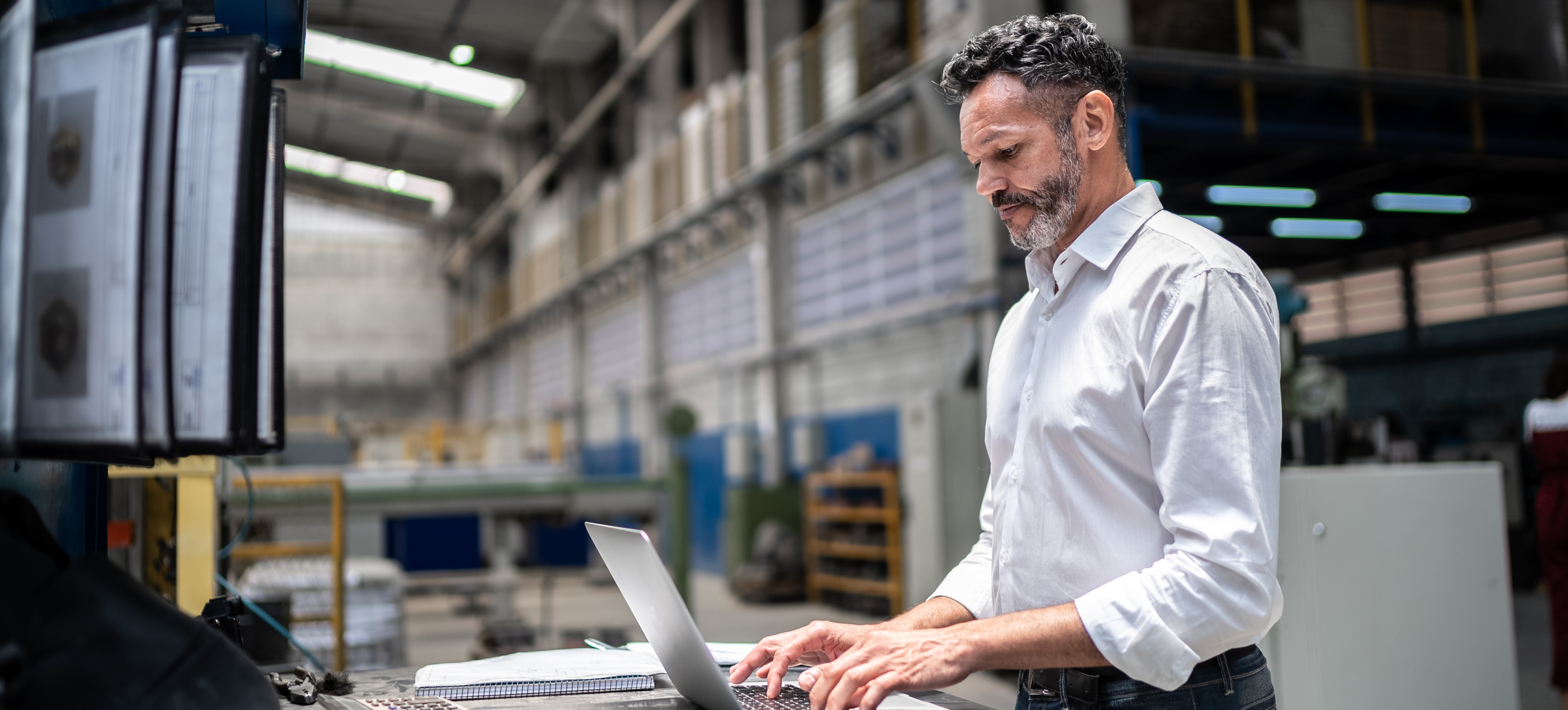 [Featured Image]: A supply chain analyst works on a laptop while standing in a warehouse.
