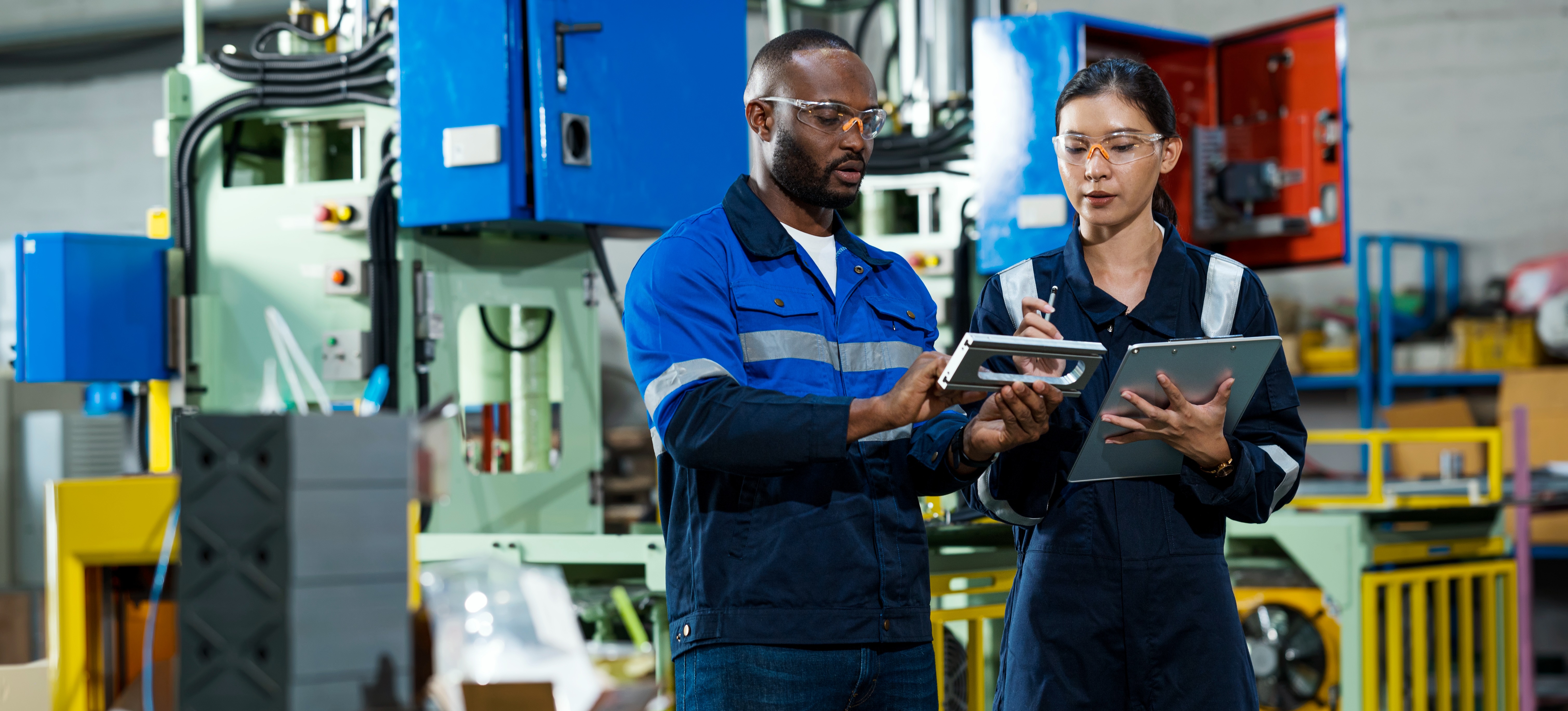 [Featured Image] Quality control engineers standing near the production line and discussing engineering parts to ensure products adhere to quality standards.
