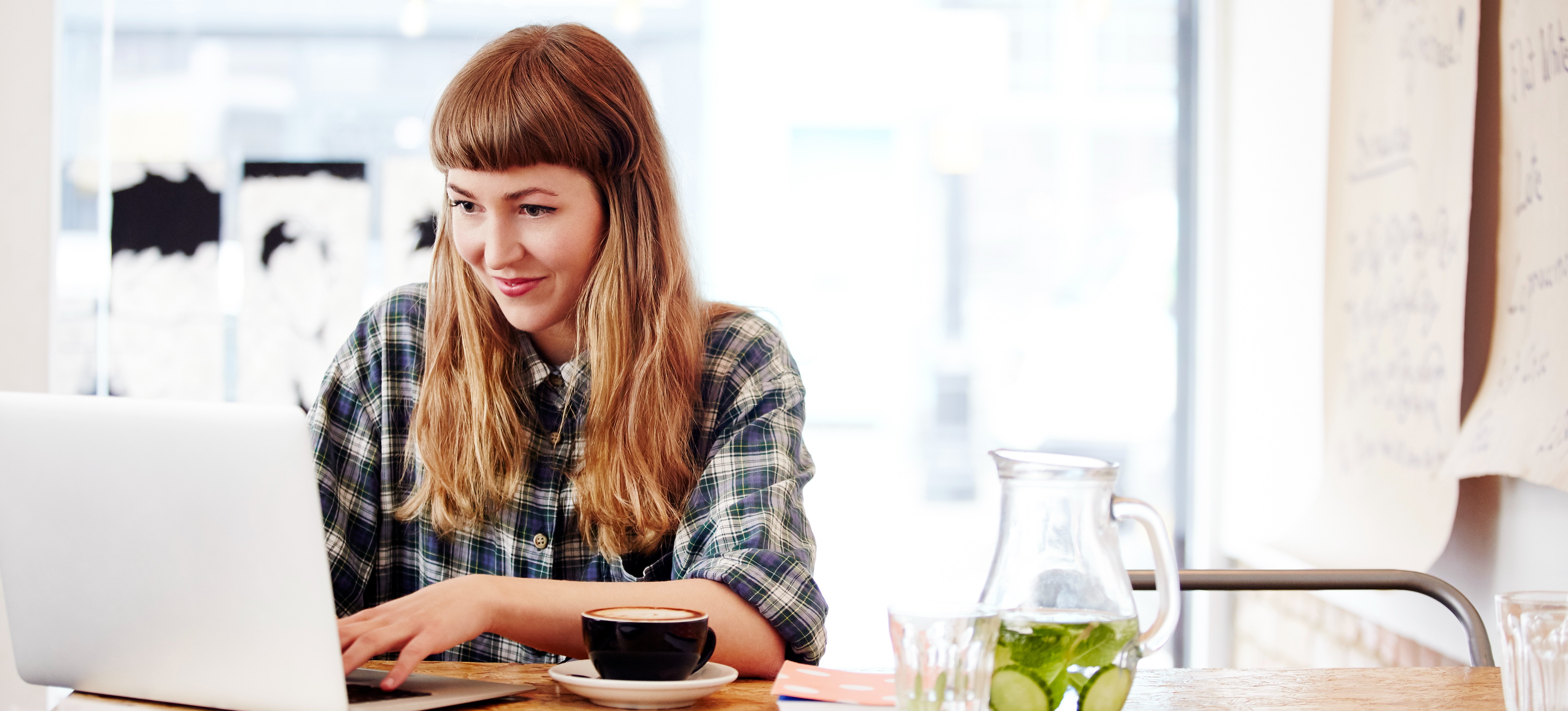 [Featured Image] A woman working at a laptop in a coffee shop uses a free portfolio website to build out a portfolio to attract clients and employers.

