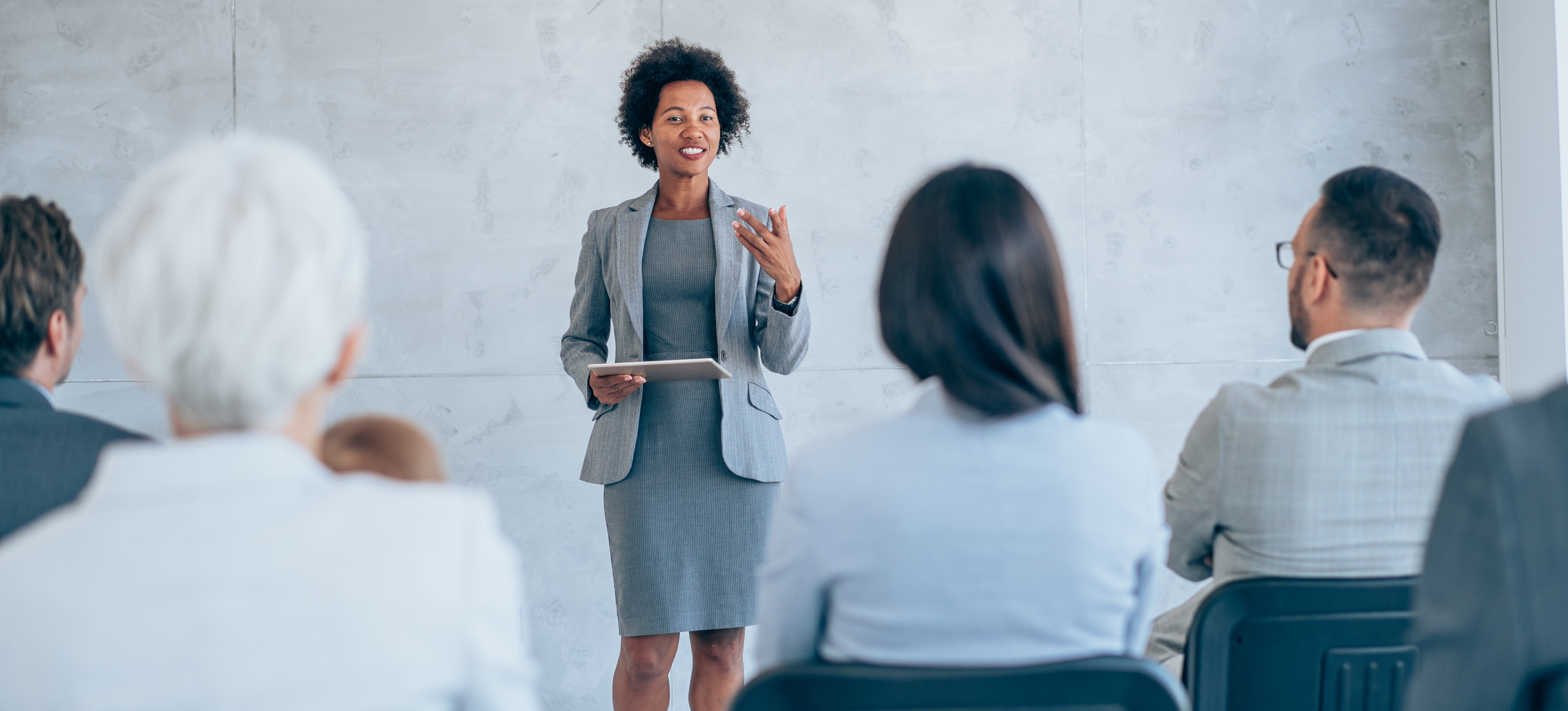 [Image en vedette] Un cadre supérieur souriant tient un appareil électronique et dispense une formation en entreprise à un groupe d'employés.