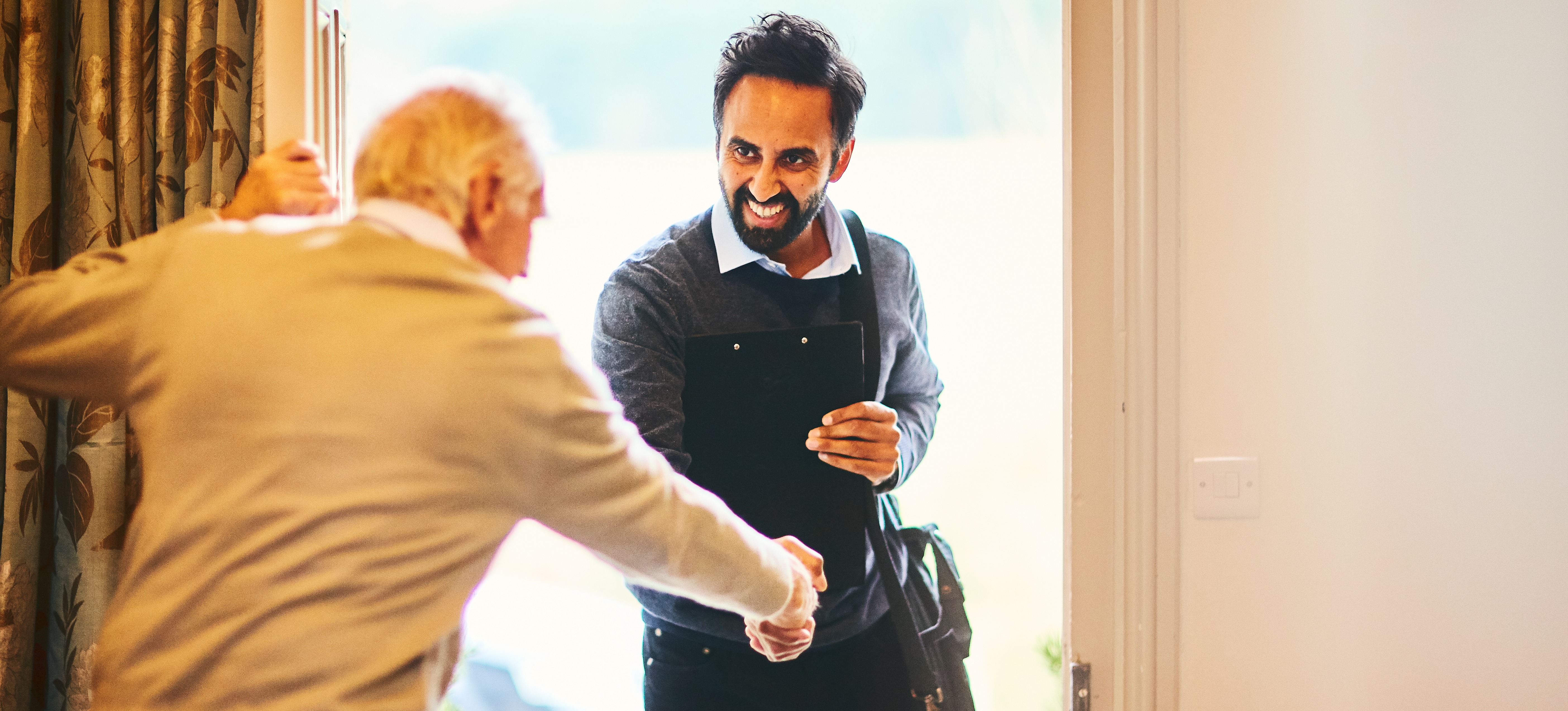 [Featured Image] A senior citizen welcoming a social worker into their home.
