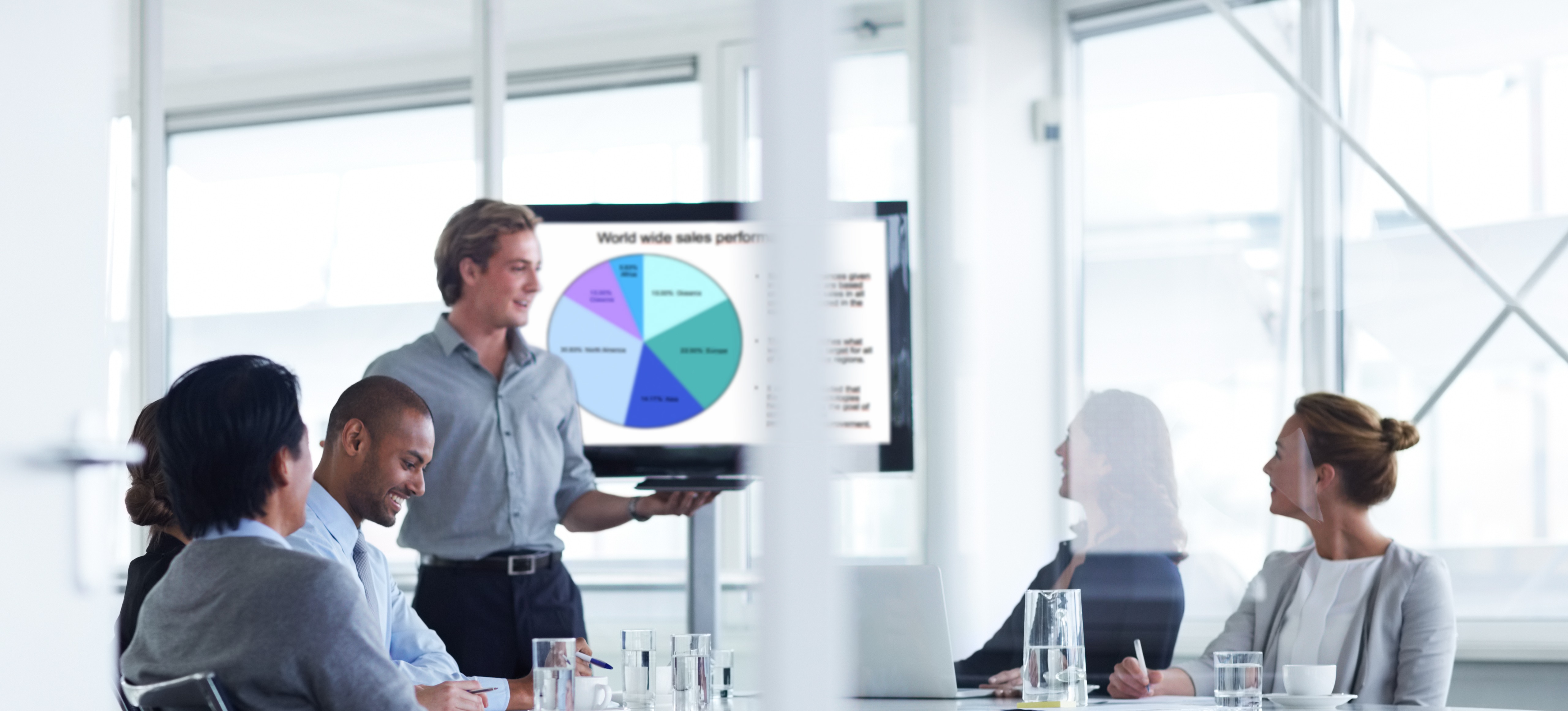 [Featured image] A product promoter is wearing a blue shirt and standing in front of a screen that shows a pie chart. They are conducting a meeting as they promote the latest product being offered.  