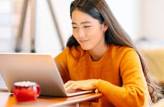 [Featured image] A cloud engineer wearing a bright orange sweater works at her laptop with a hot beverage in a bright office or cafe.