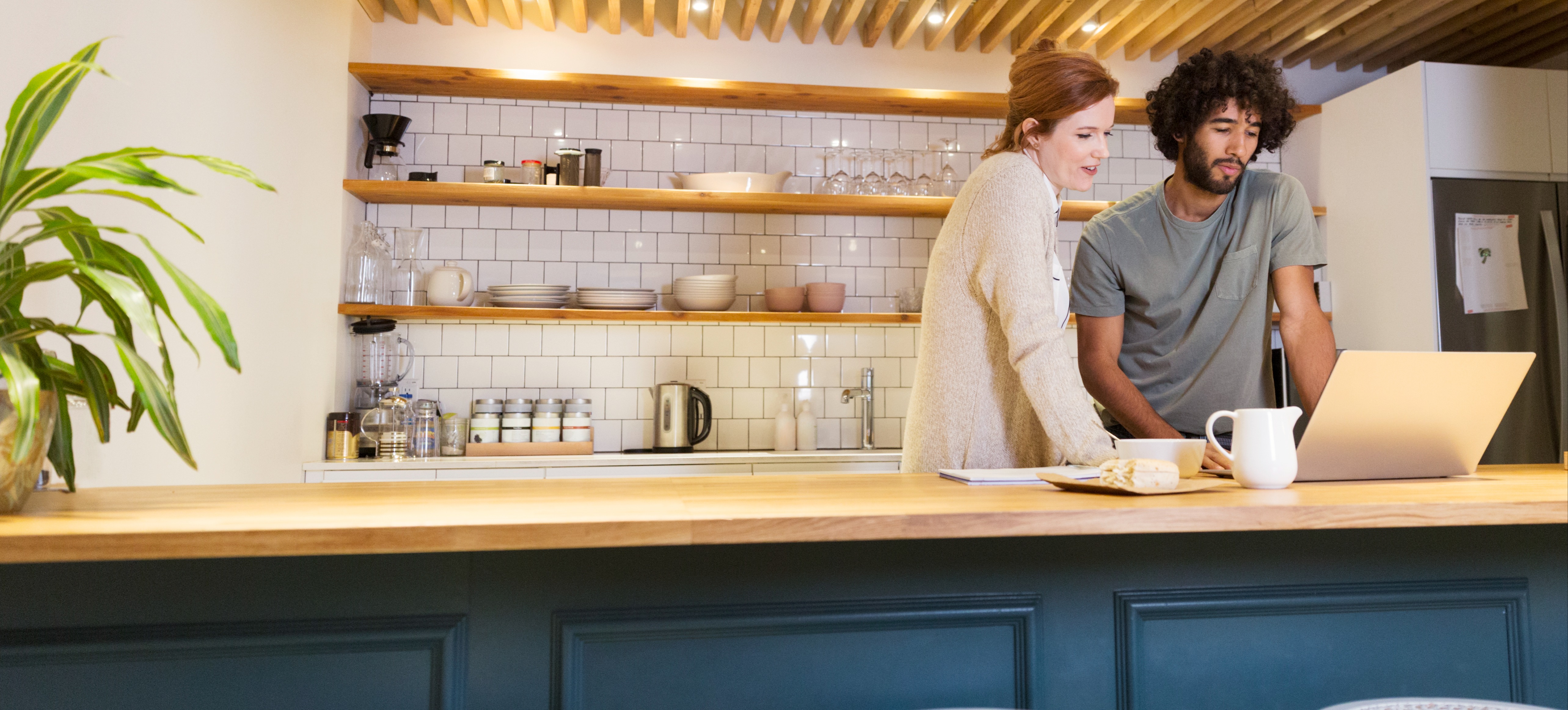 [Featured Image] A young couple of entrepreneurs stand at a counter with a laptop to discuss small business ideas