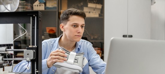 [Featured Image] An Oculus developer holds a headset while looking at their computer.
