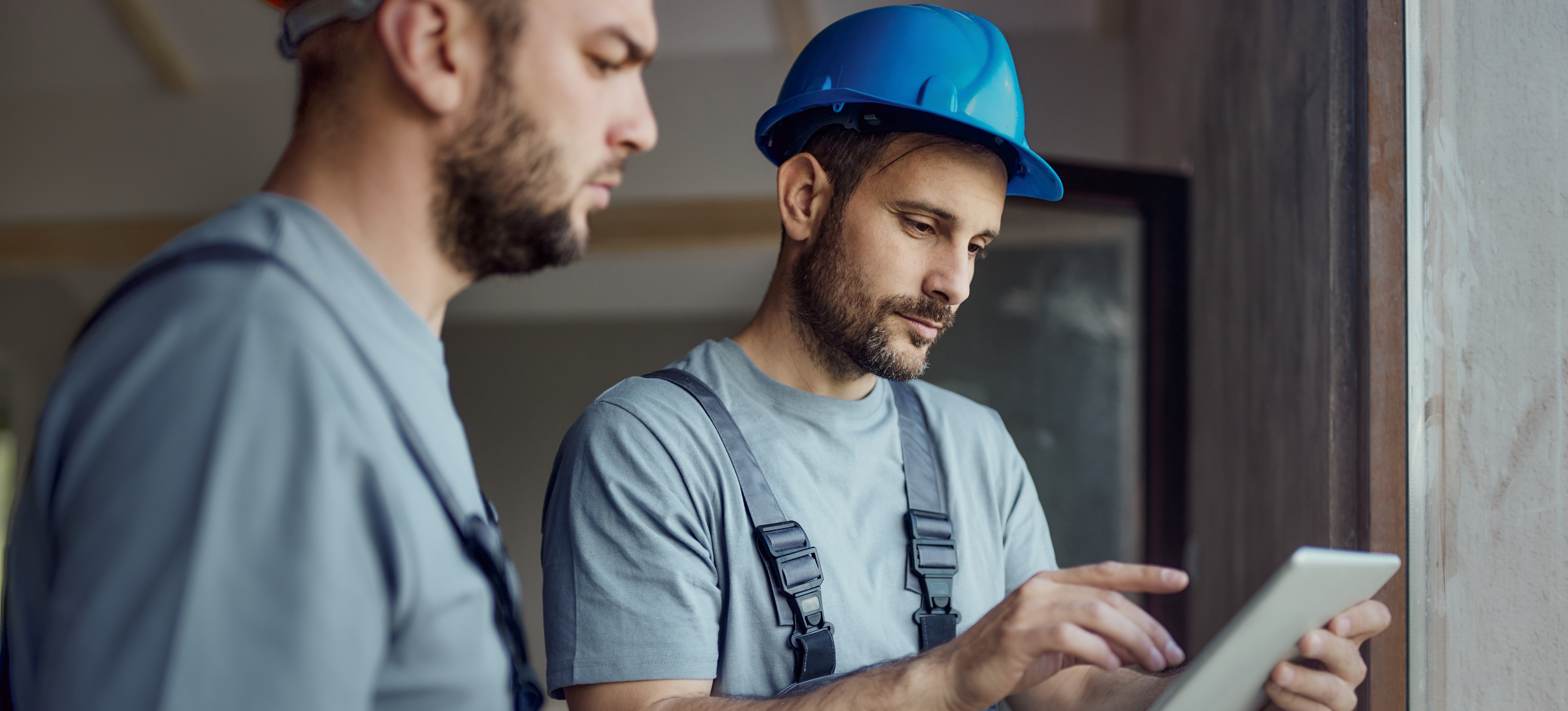[Featured Image] A construction manager looks at a tablet and explains a project to a colleague on a construction site. ﻿