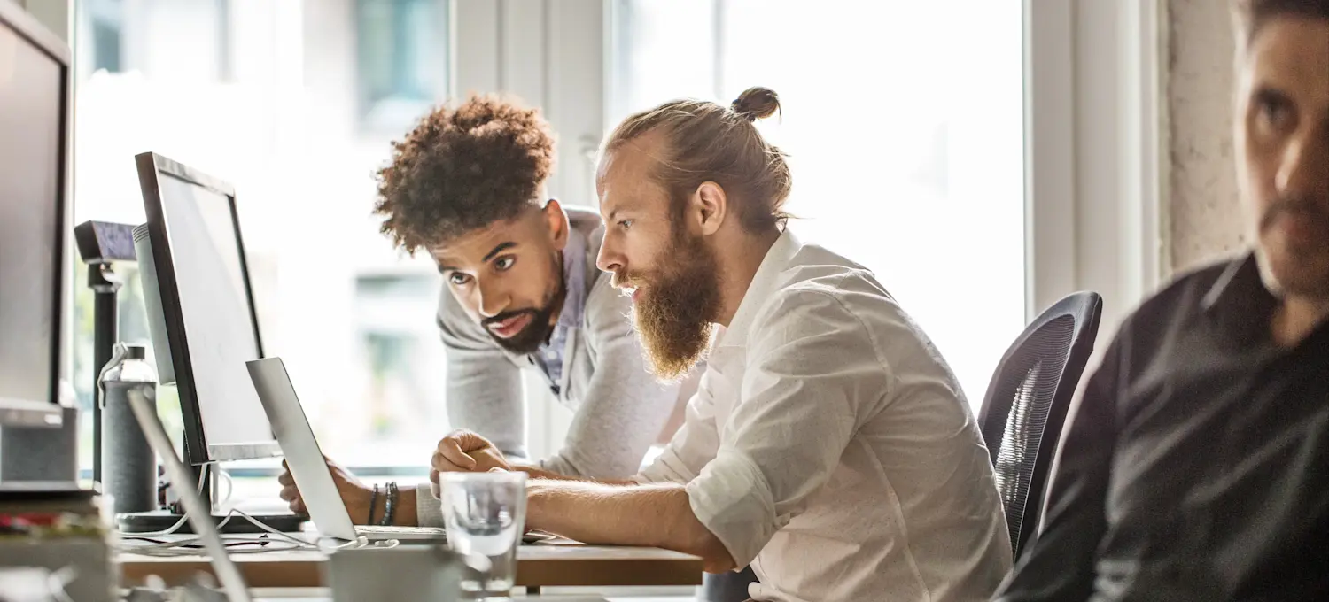 [Featured Image] Two software developers sit at a computer and review information for their public sector cybersecurity jobs.
