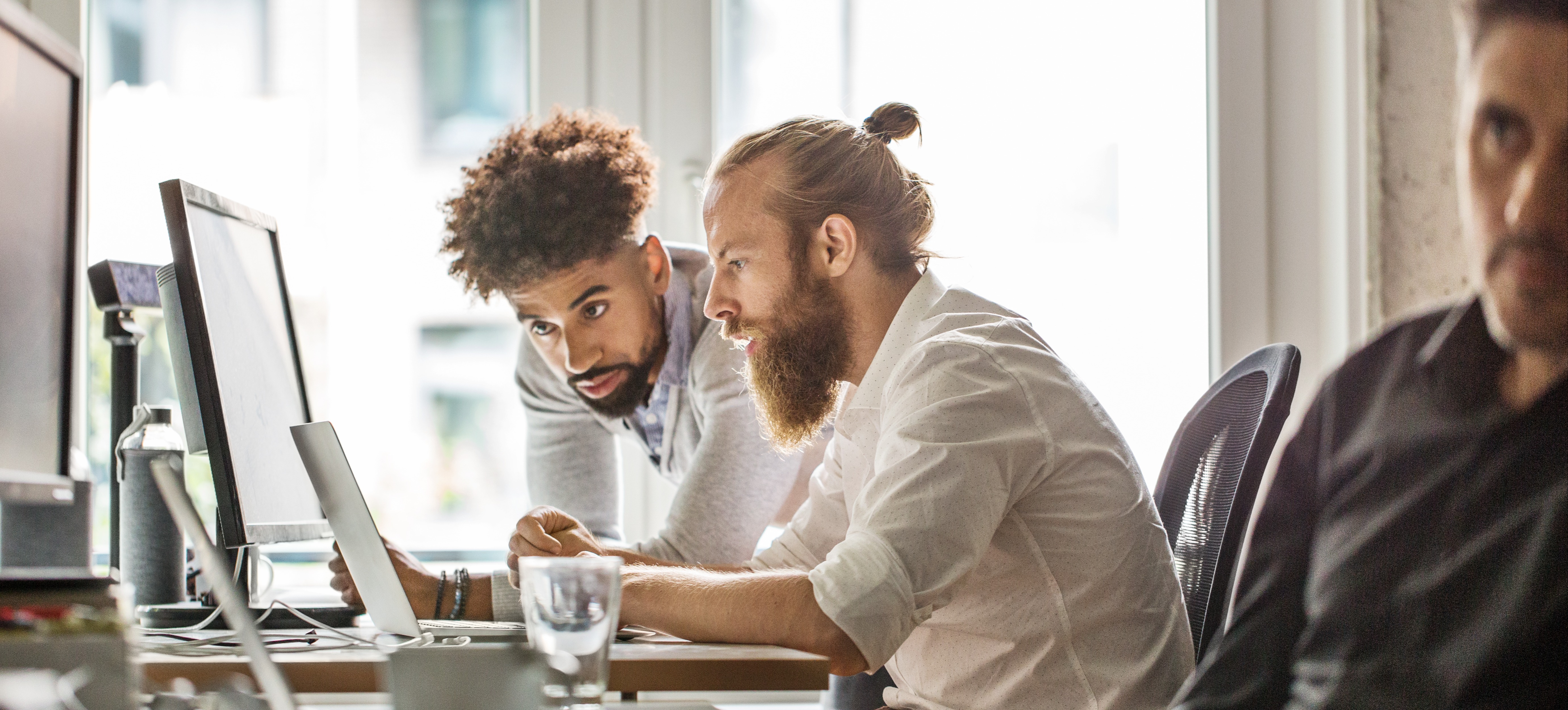 [Featured Image] Two software developers sit at a computer and review information for their public sector cybersecurity jobs.

