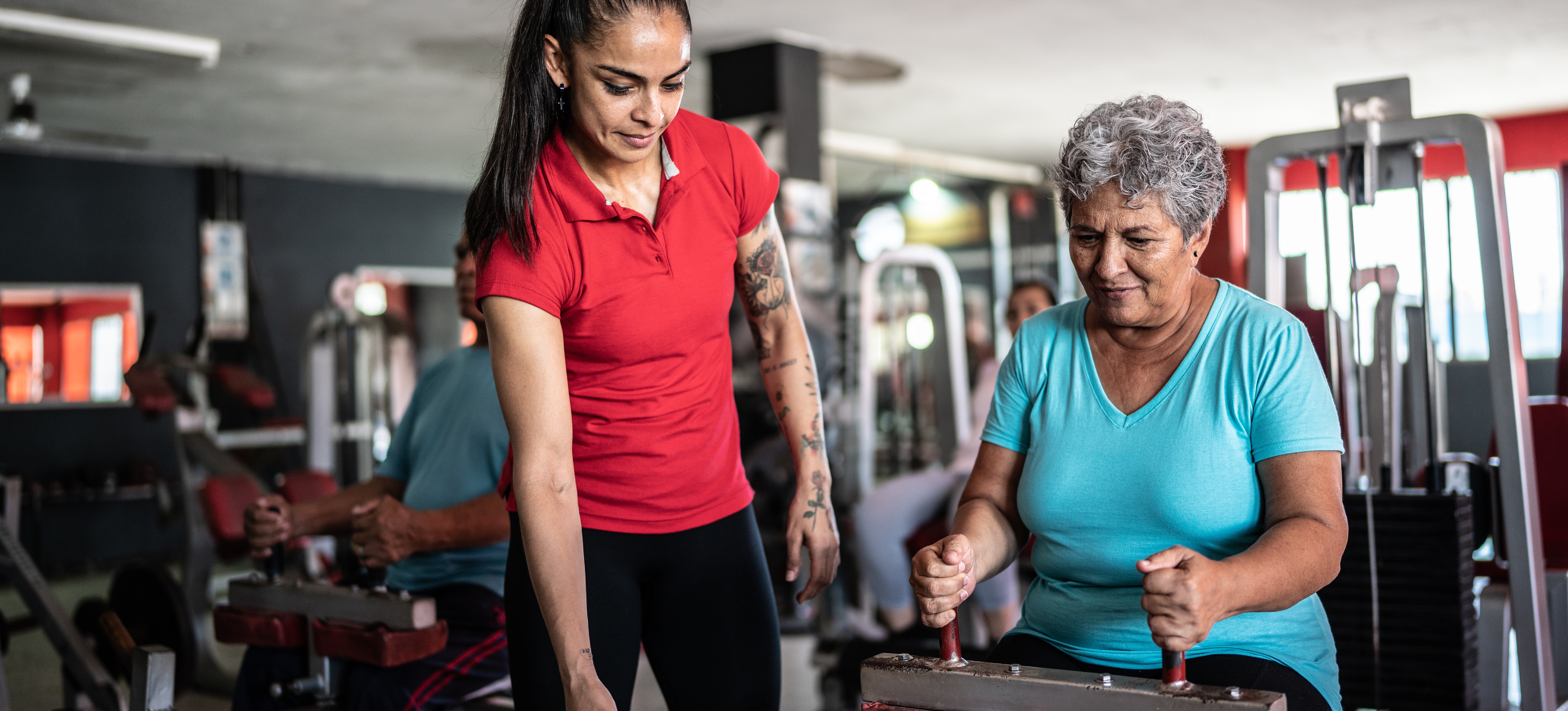 [Featured Image] A personal trainer shows a client how to use an exercise machine in a gym.  
