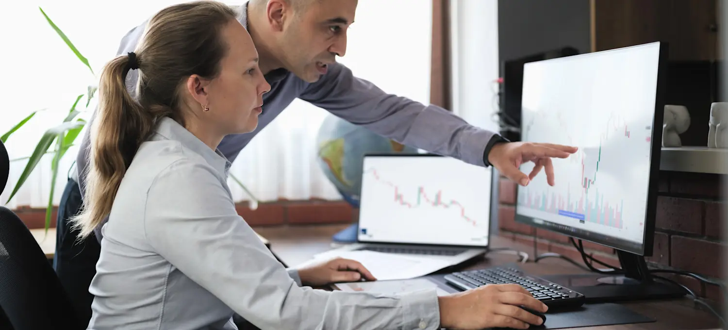 [Featured Image]: A crypto analyst and a colleague work together in an office, analyzing cryptocurrency charts and data.
