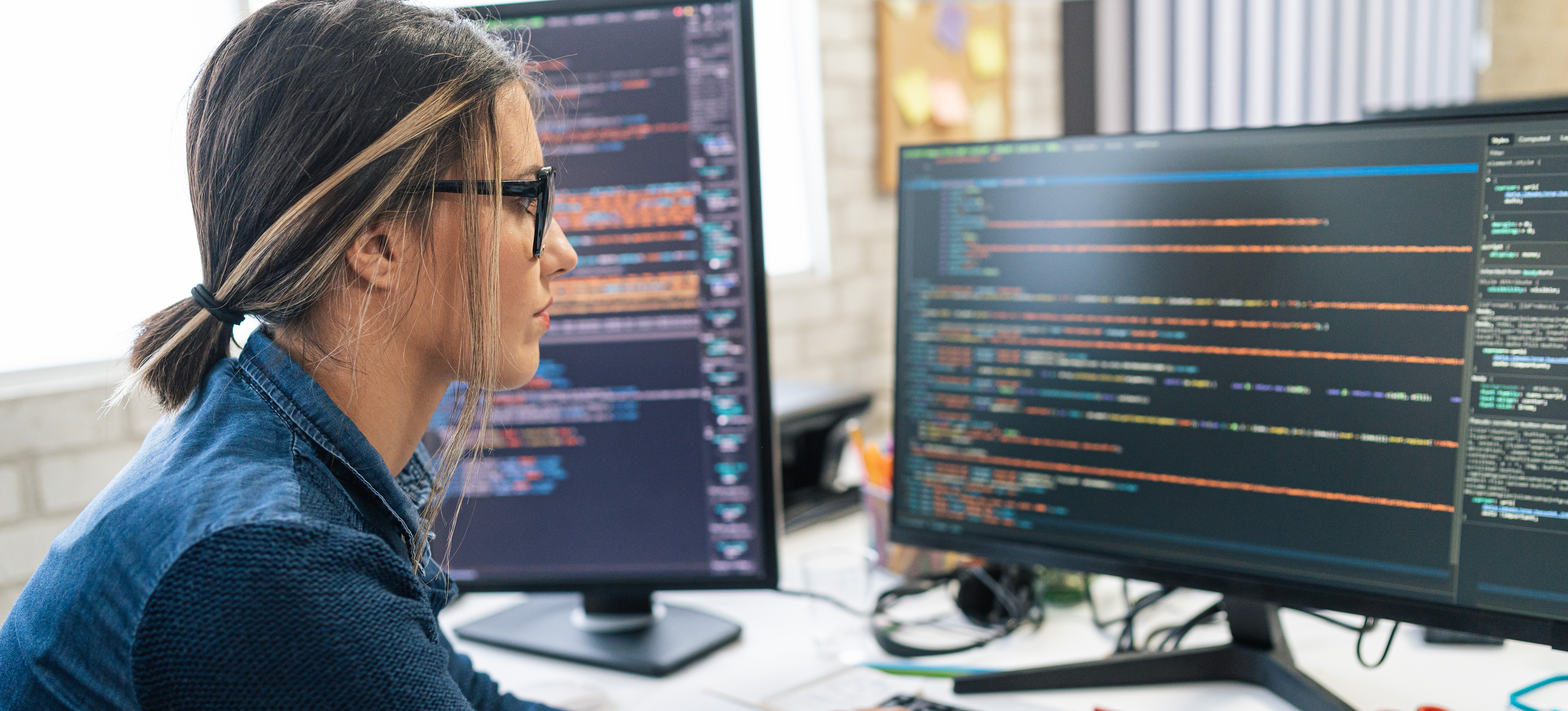 [Featured Image] A web developer, which is one of the highest-paying tech jobs, works on some coding on a computer with two screens.
