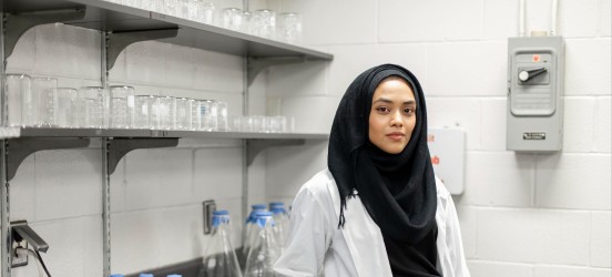 [Featured Image]:  A toxicologist, wearing a white lab coat, head covering and blue gloves is working in the laboratory. 