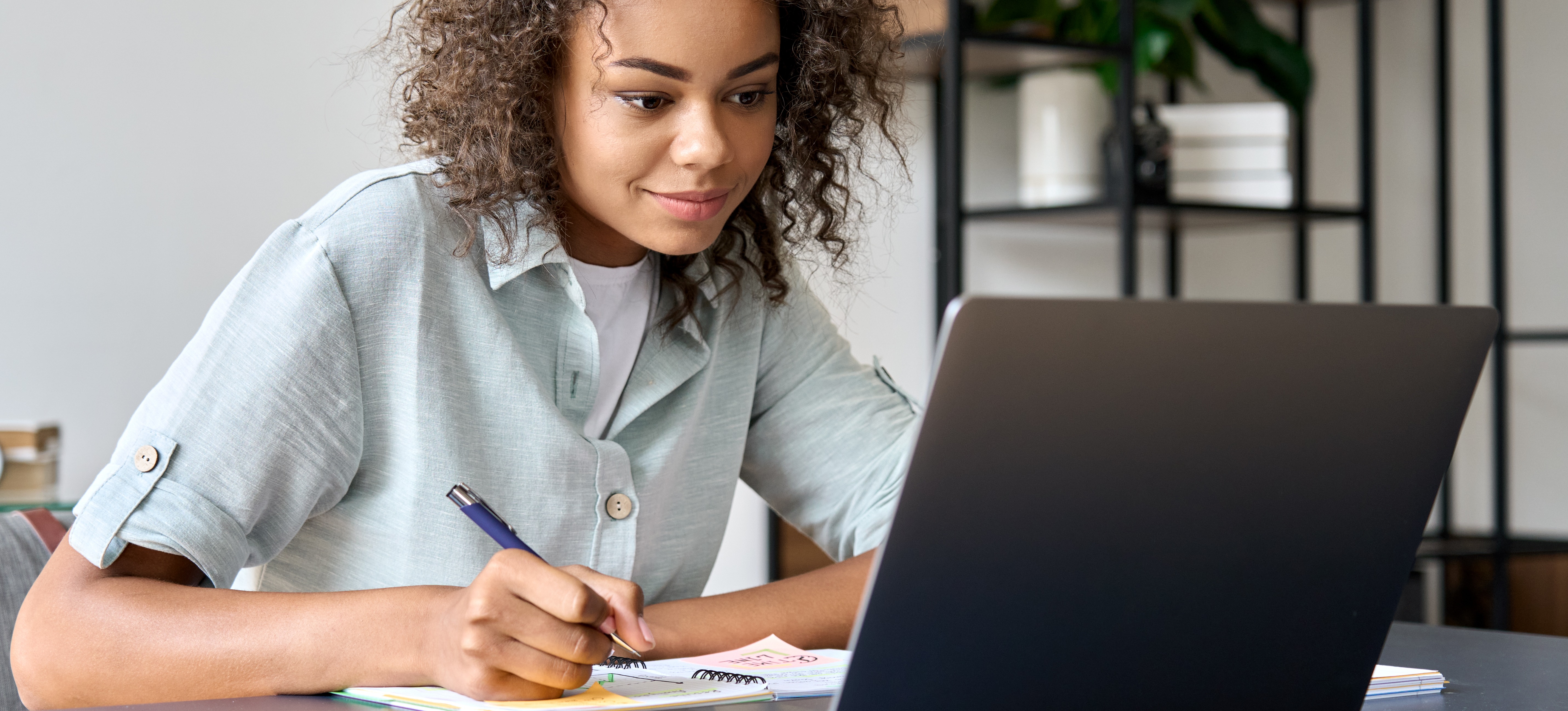 [Featured image] A person works on college essay topics with a pen, notebook, and laptop computer.