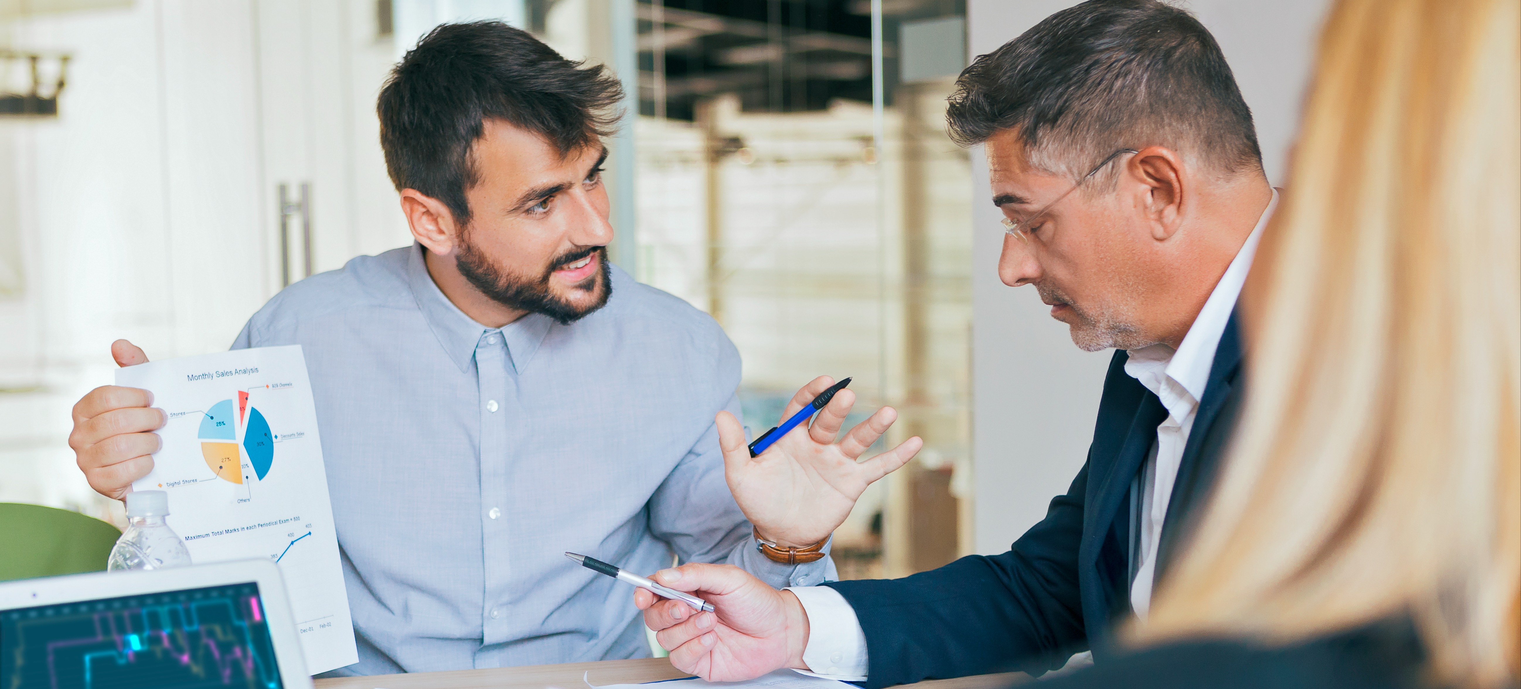 [Featured Image] A man in a saas sales meeting shows a sales sheet to a potential client seated next to him.

