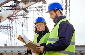 [Featured Image] Two project engineers work at a construction site and look at documentation for their project.