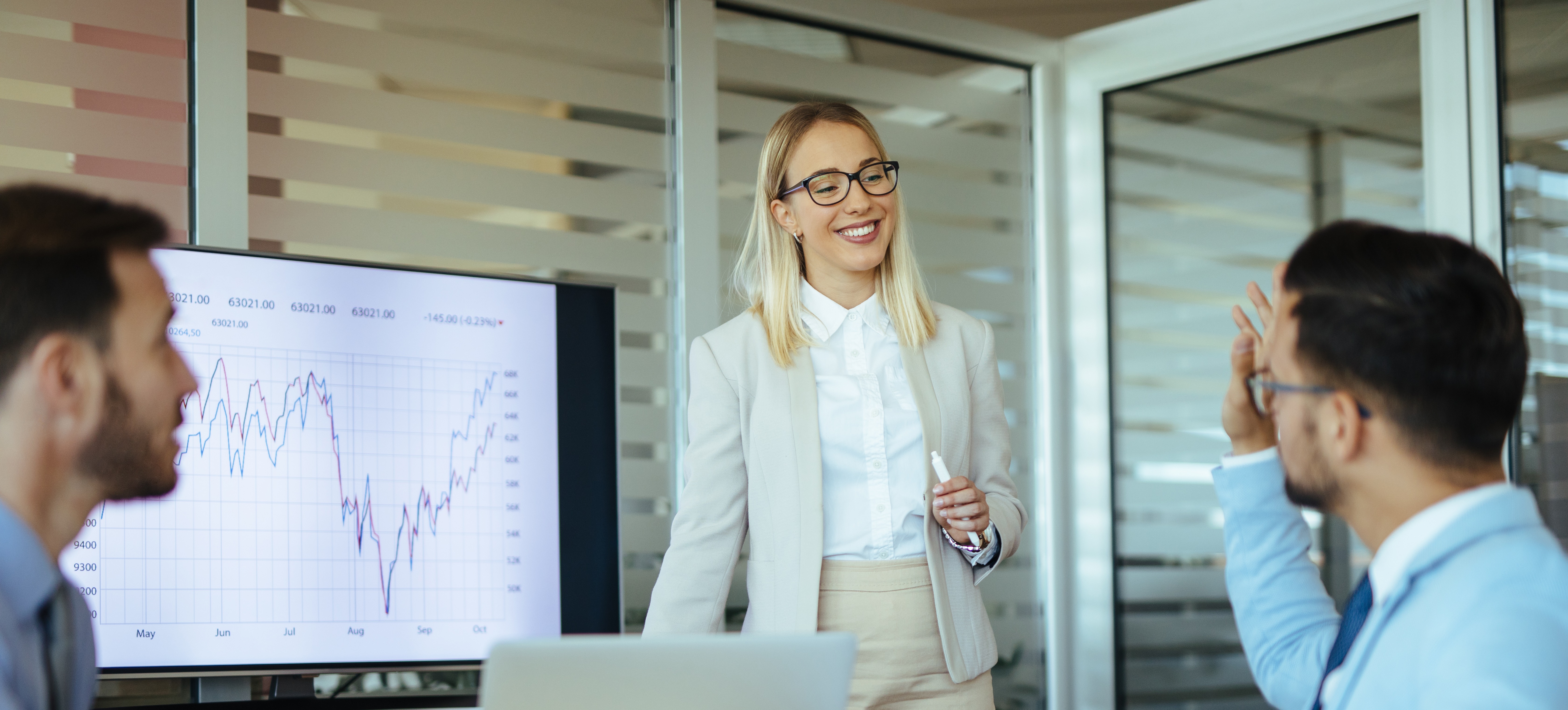 [Featured image] A person with blonde hair and wearing a white jacket is running a meeting with charts and a computer, with a colleague in a blue jacket and glasses and a person with a beard.