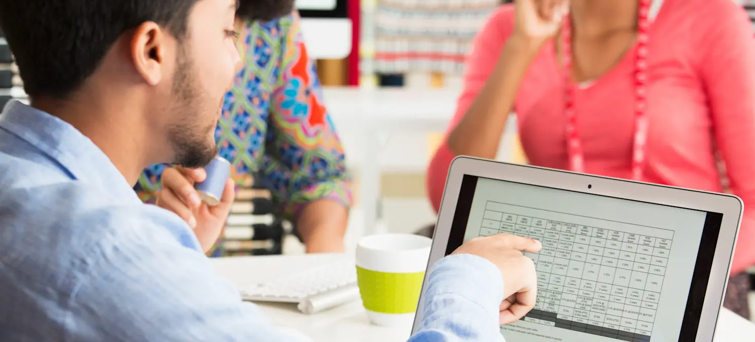 [Featured Image] A business person explains spreadsheet data created with DAX for Power BI to their project team members.