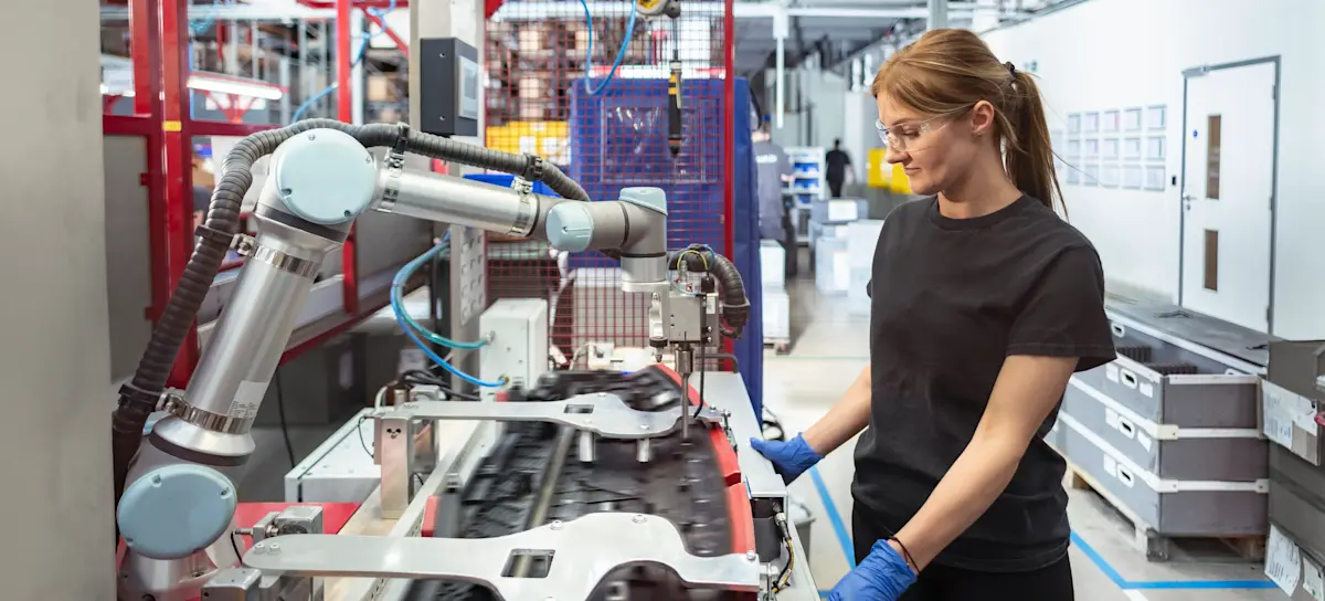 [Featured Image] A person in a manufacturing plant works with a cobot, which is an example of using AI in production.
