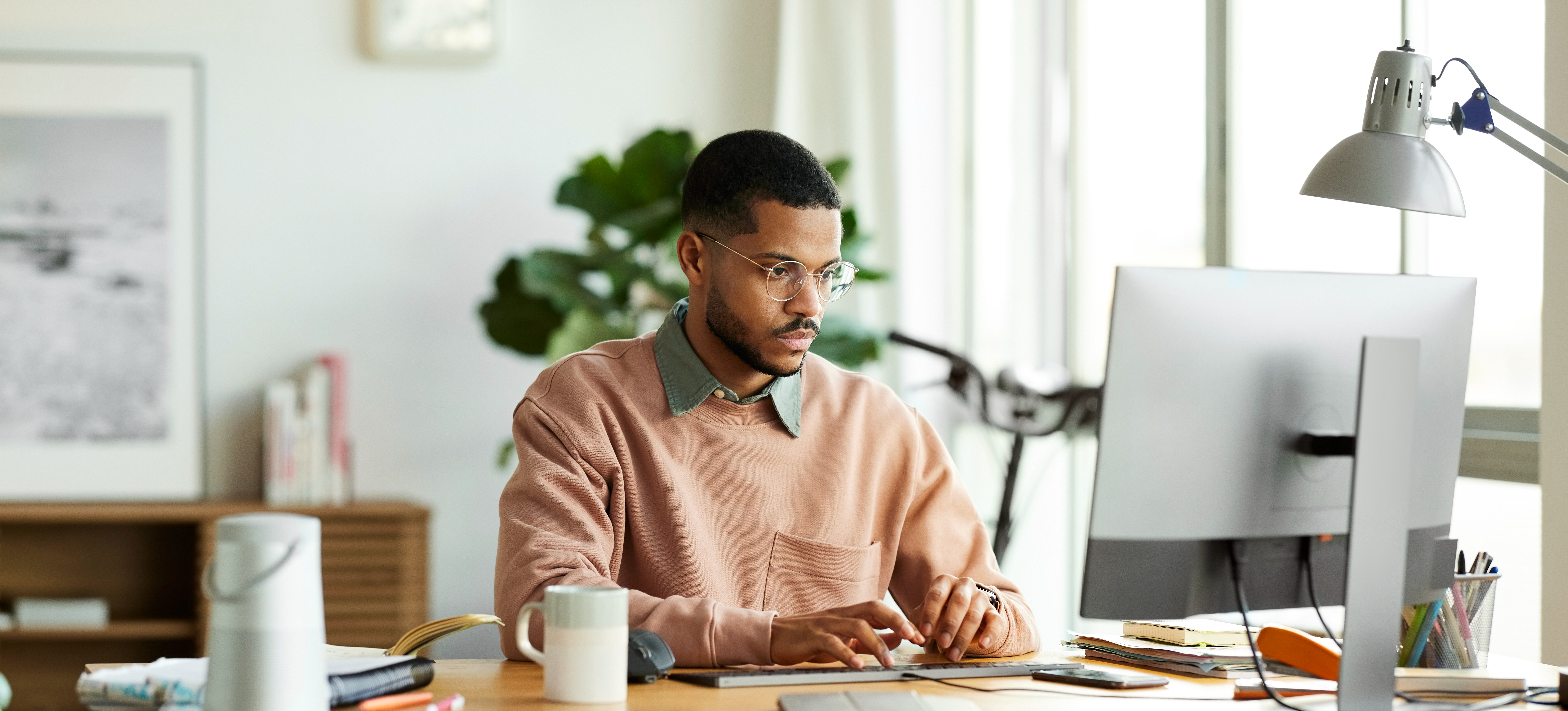 [Image en vedette] Un homme d'affaires travaille sur son ordinateur de bureau dans un bureau avec beaucoup de lumière naturelle pendant qu'il apprend les fonctions de Google Sheets pour l'aider à accomplir ses tâches.