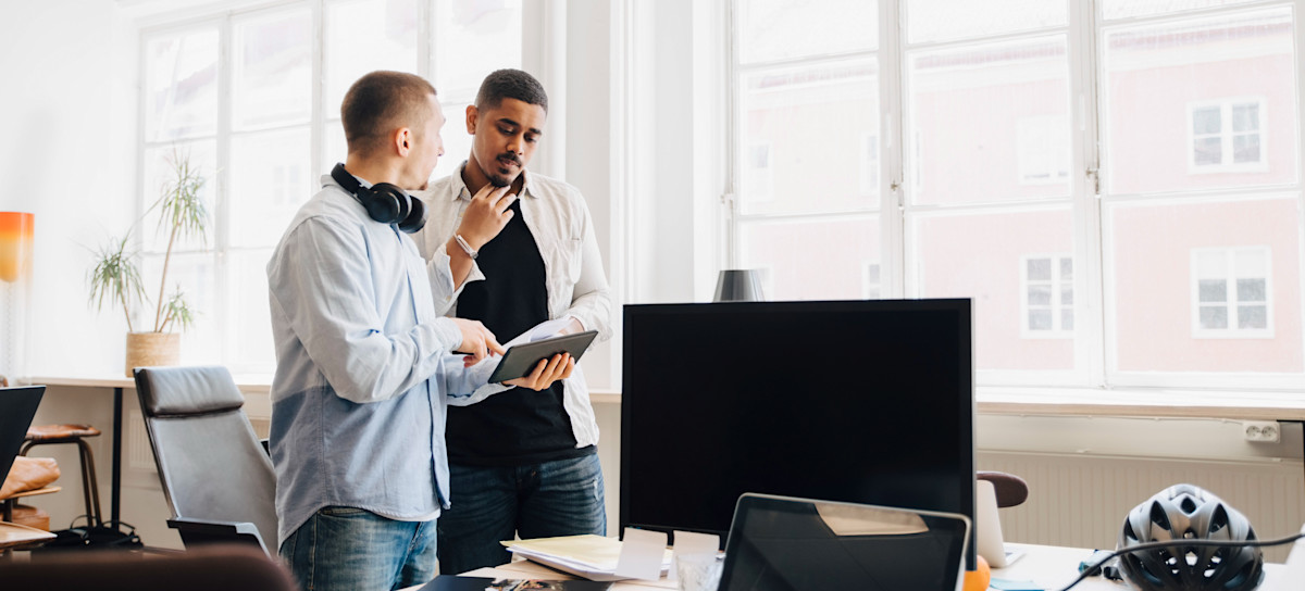 [Featured Image] Colleagues discuss the differences between a router and a modem while searching for answers on their tablets.
