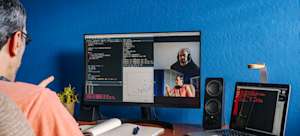 [Featured Image] A programmer examines code while on a video call with other members of his coding team.