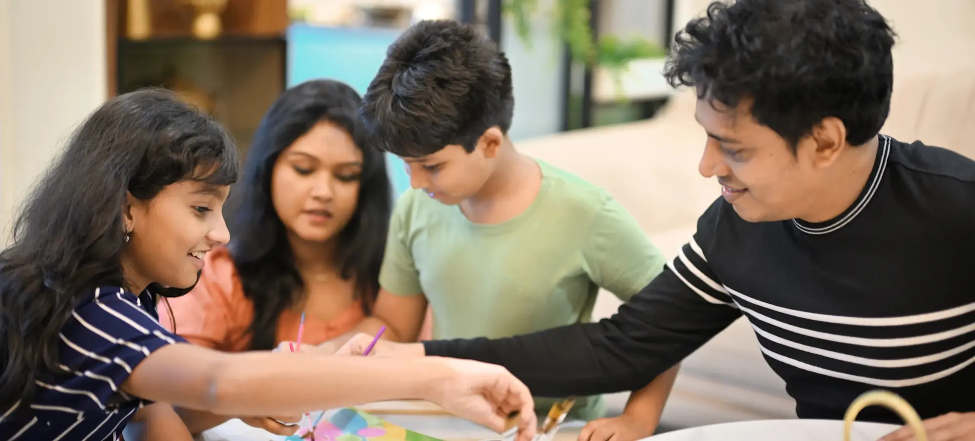 [Featured Image] A family of four does activities together around coffee tables thanks to working jobs for better work-life balance, each offering ample time to enjoy with loved ones. 
