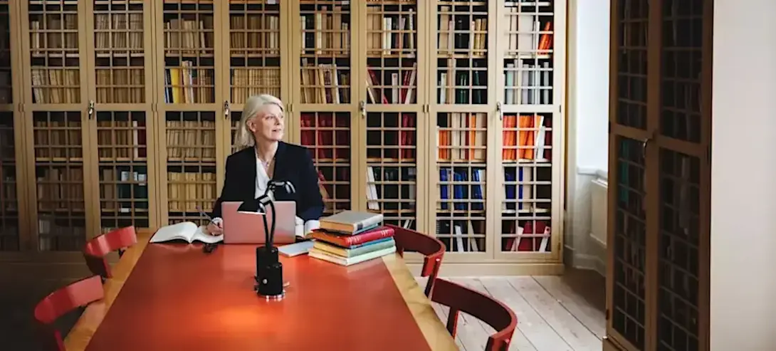 [Featured Image] A person attending law school is sitting at a library table with a stack of books and a laptop computer