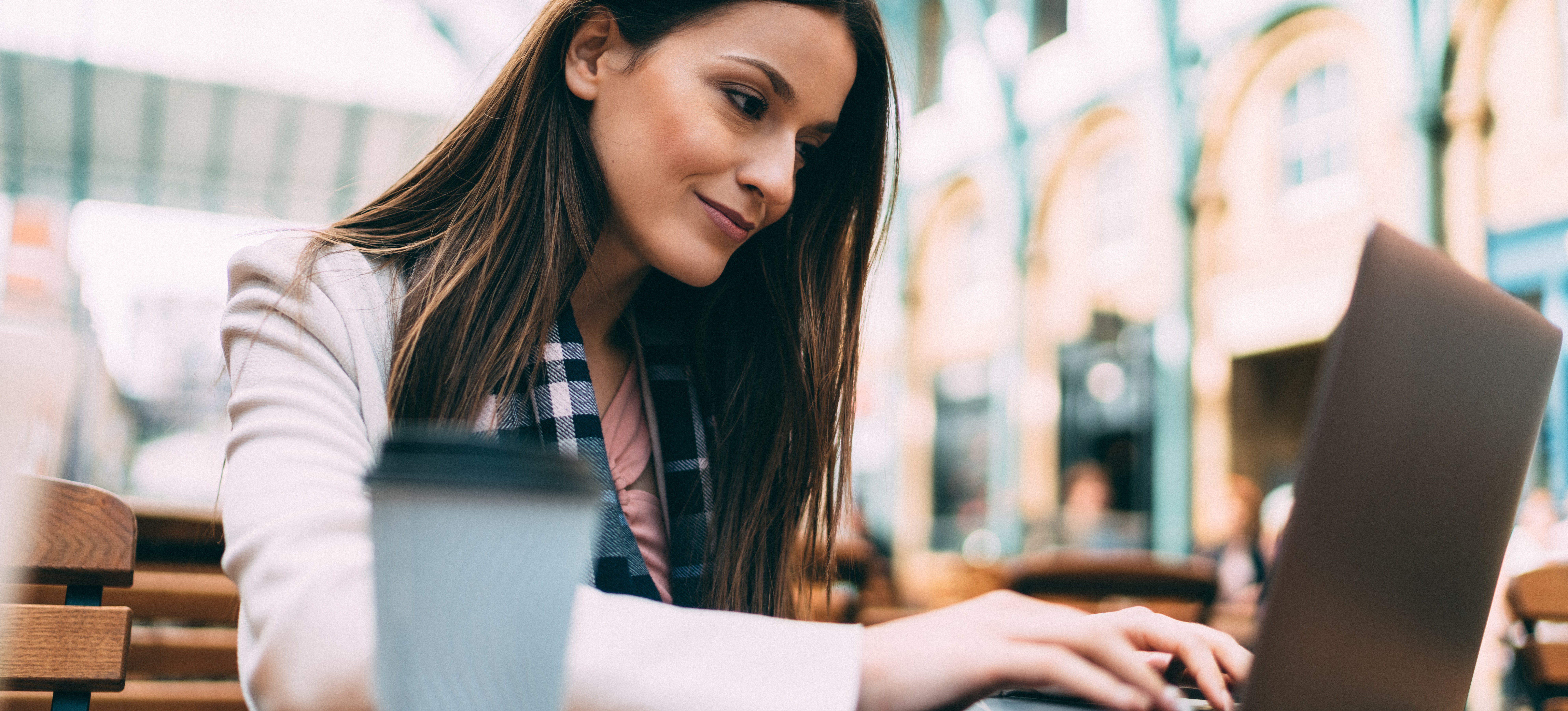 [Featured Image] A penetration tester sits outdoors with a cup of coffee and uses their laptop to look for potential cybersecurity financial sector jobs. 
